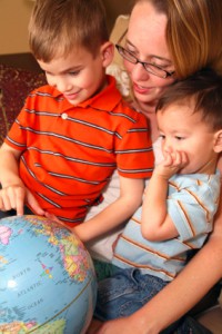young mother examining a globe with her two pre-school aged sons