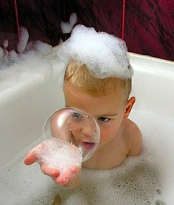 three-year-old gazes intently into bathtub bubble