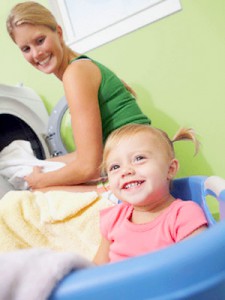 Toddler girl happily watches her mother unload a clothes dryer