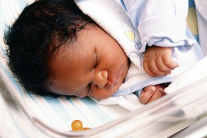 A newborn African-American baby is depicted asleep in a pediatric intensive care unit.