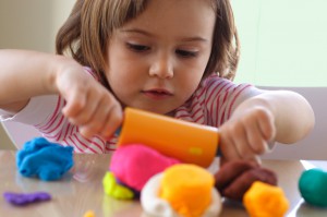 three-year-old girl diligently rolling out modeling clay